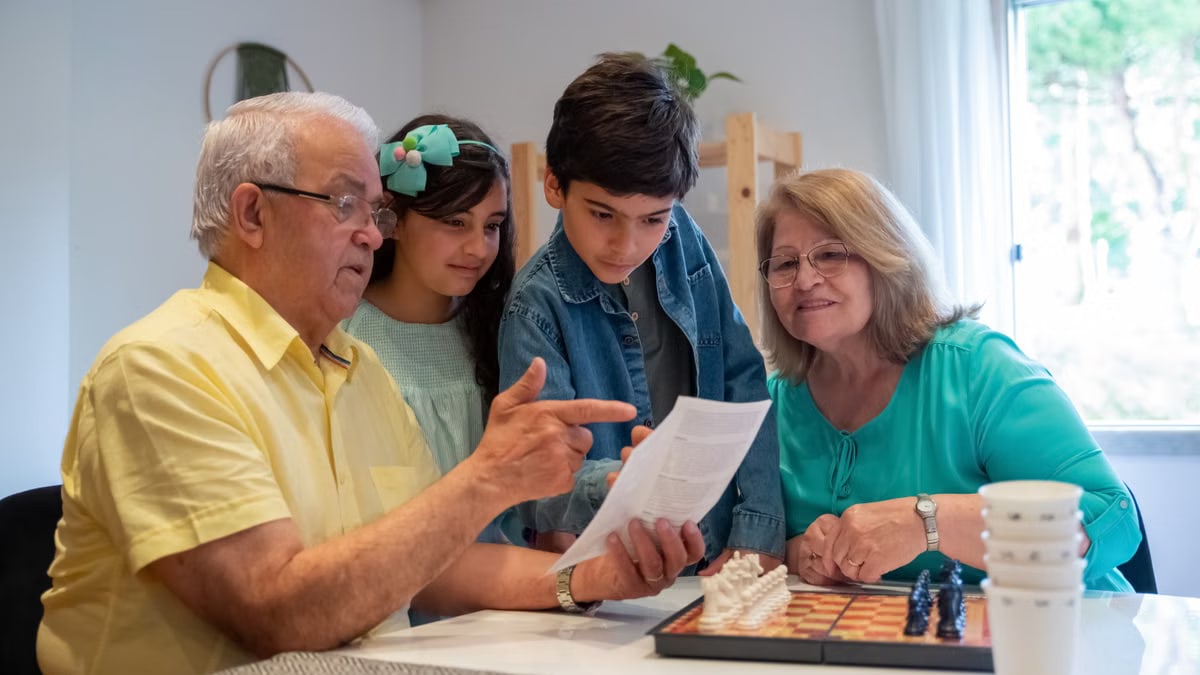 Grandparents teaching grandchildren to play chess in a cozy home setting.