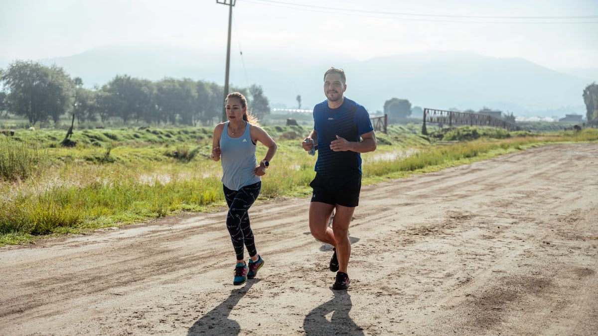 Active couple jogging on a dirt road in a scenic rural area under the bright sun.